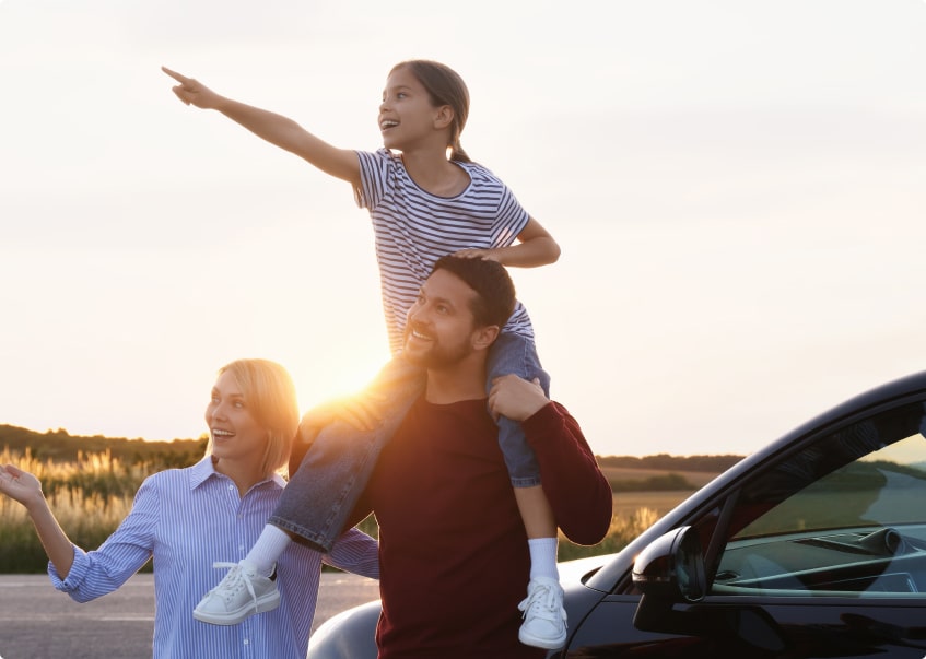 family of 3 standing by their car pointing at something